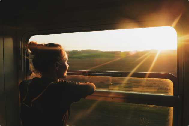 Passenger looking through a train window at sunset